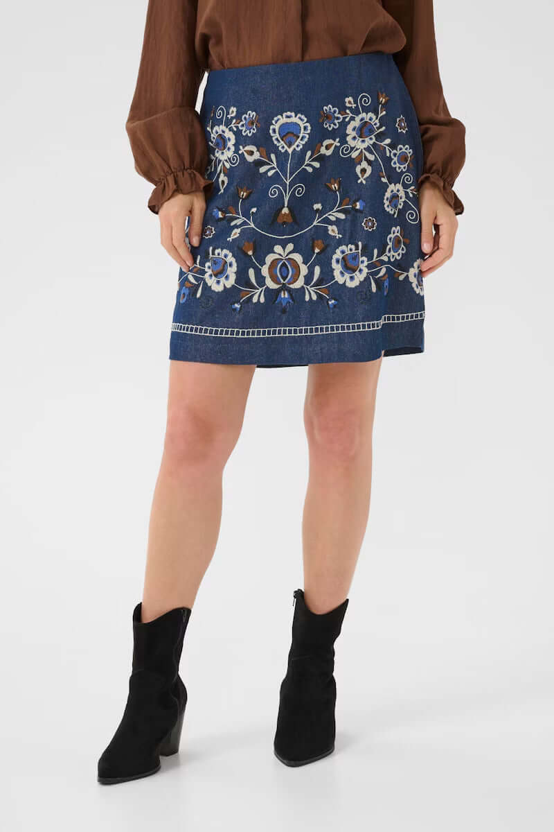 Femme portant Jupe Gro en denim avec broderies florales, coupe droite au-dessus du genou, style bohème chic.