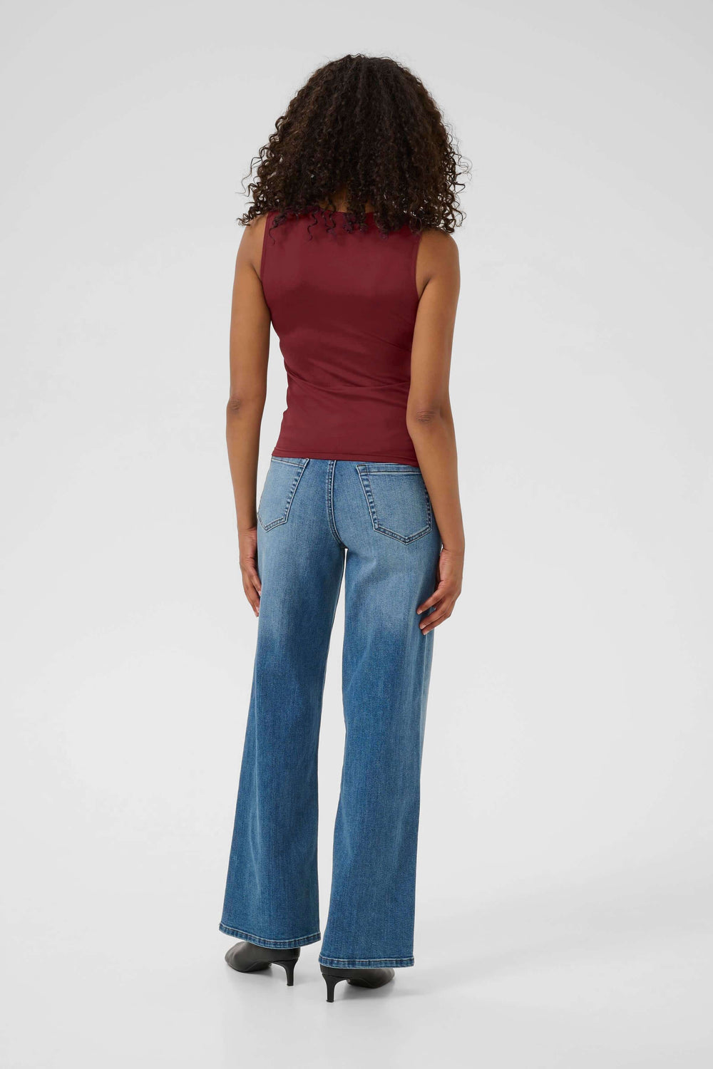 Mode femme portant un haut sans manches rouge et un jean évasé. Vue arrière avec un style moderne élégant.