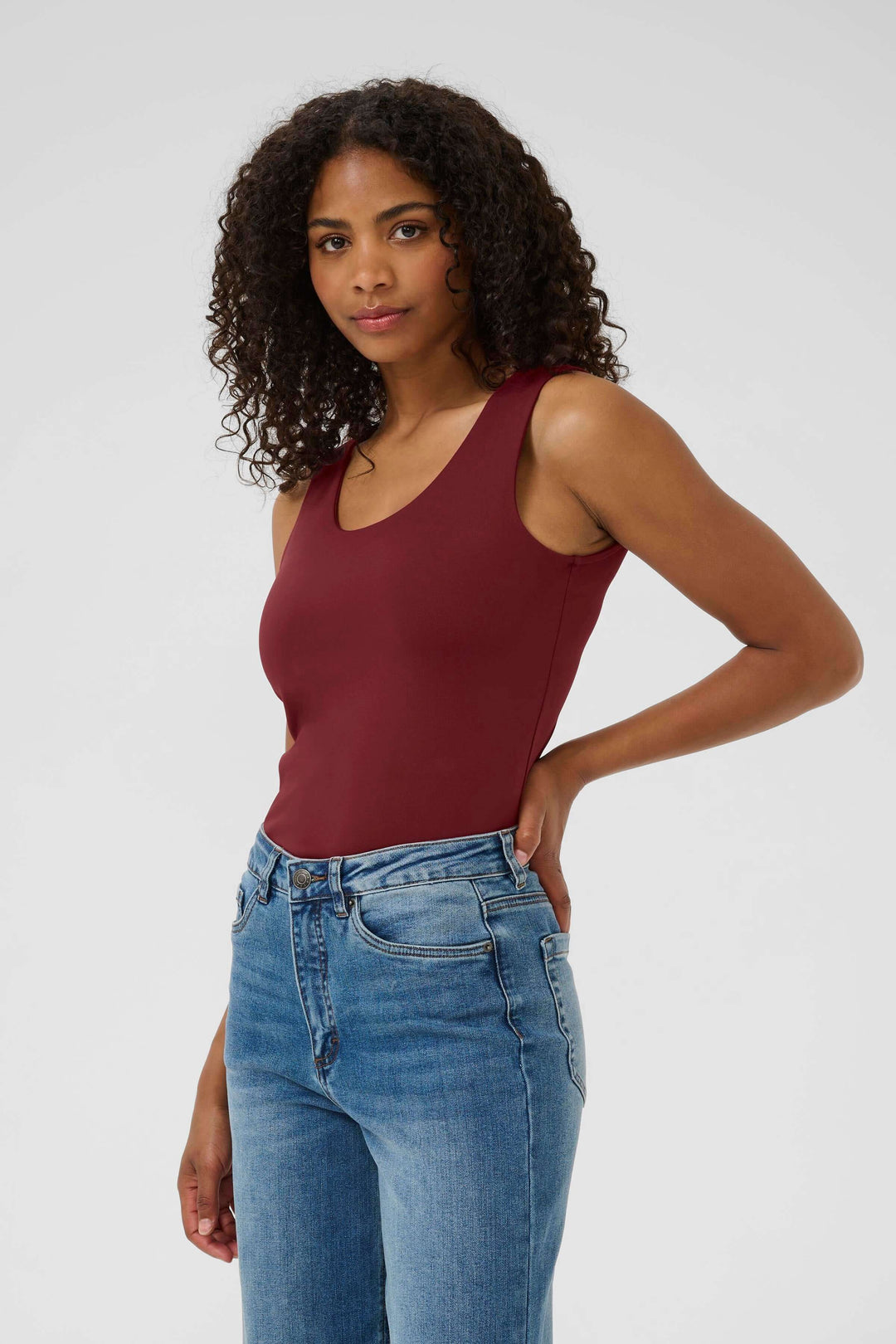 Person wearing burgundy tank top with blue jeans.