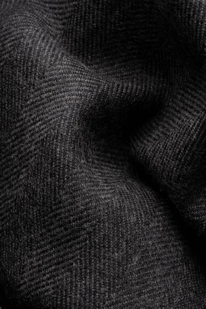 Gros plan sur un foulard en laine noir avec motif chevrons ton sur ton, texte subtil et texture raffiné.