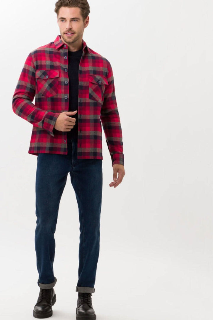 Homme portant une chemise à carreaux rouge et noir, avec un jean bleu, en style décontracté.