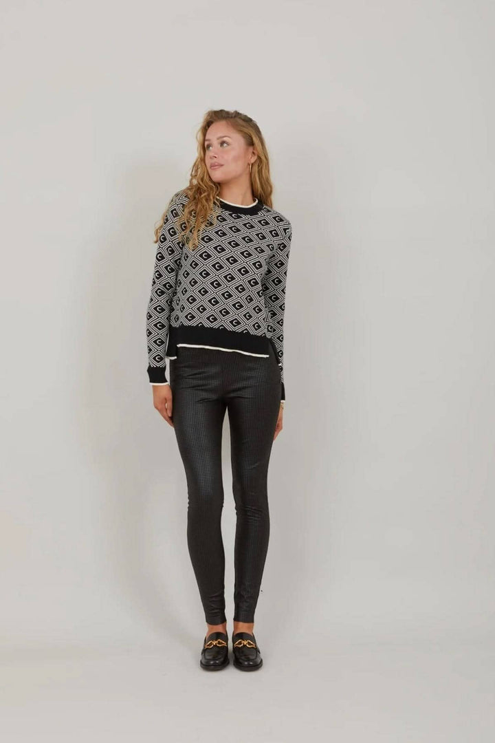 Femme portant un legging noir ajusté avec un pull à motifs gris et blanc, look chic décontracté.
