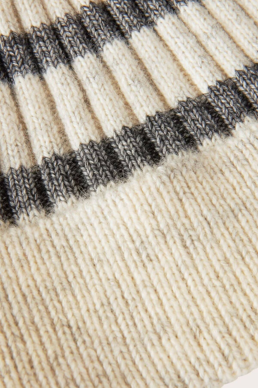 Gros plan sur un bonnet à rayures grises et crème, en tissu doux en laine et coton, parfait pour l'hiver.