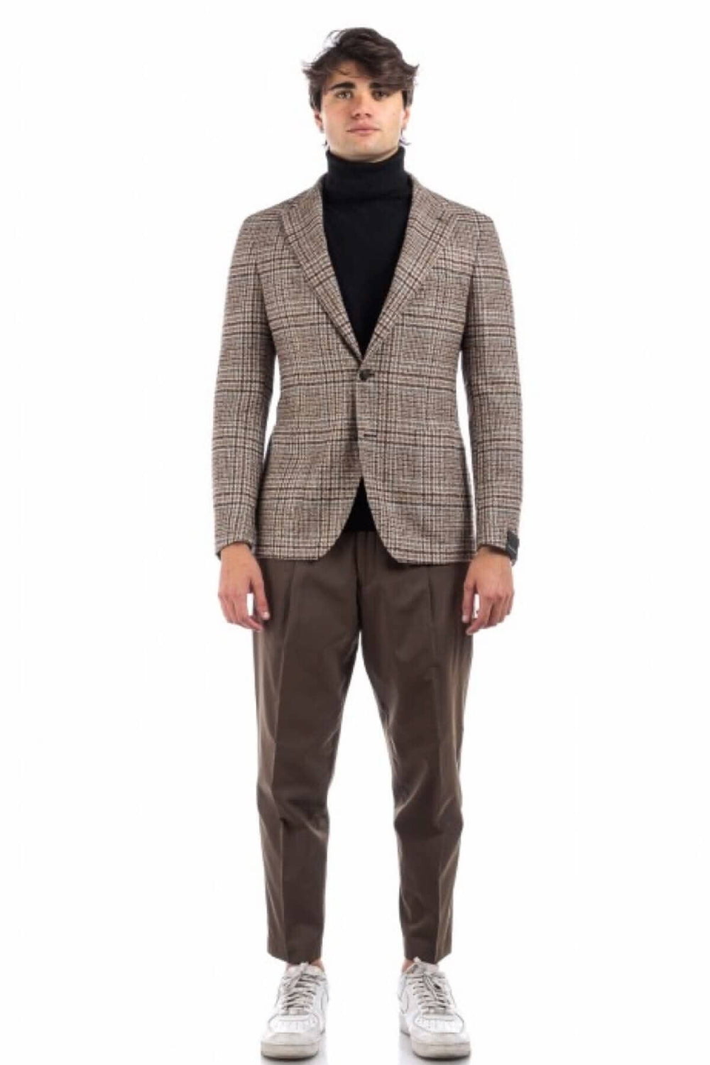 Homme portant un veston à motif pays de galles, avec un turtleneck noir et des pantalons bruns.