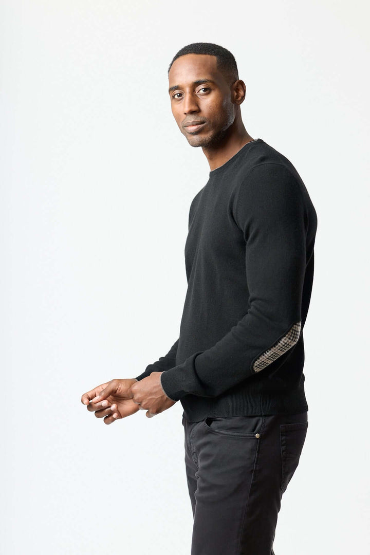 Homme portant un chandail en laine vierge et cachemire noir avec coudières pied-de-poule, élégance et confort. Décris moi le produit en français.