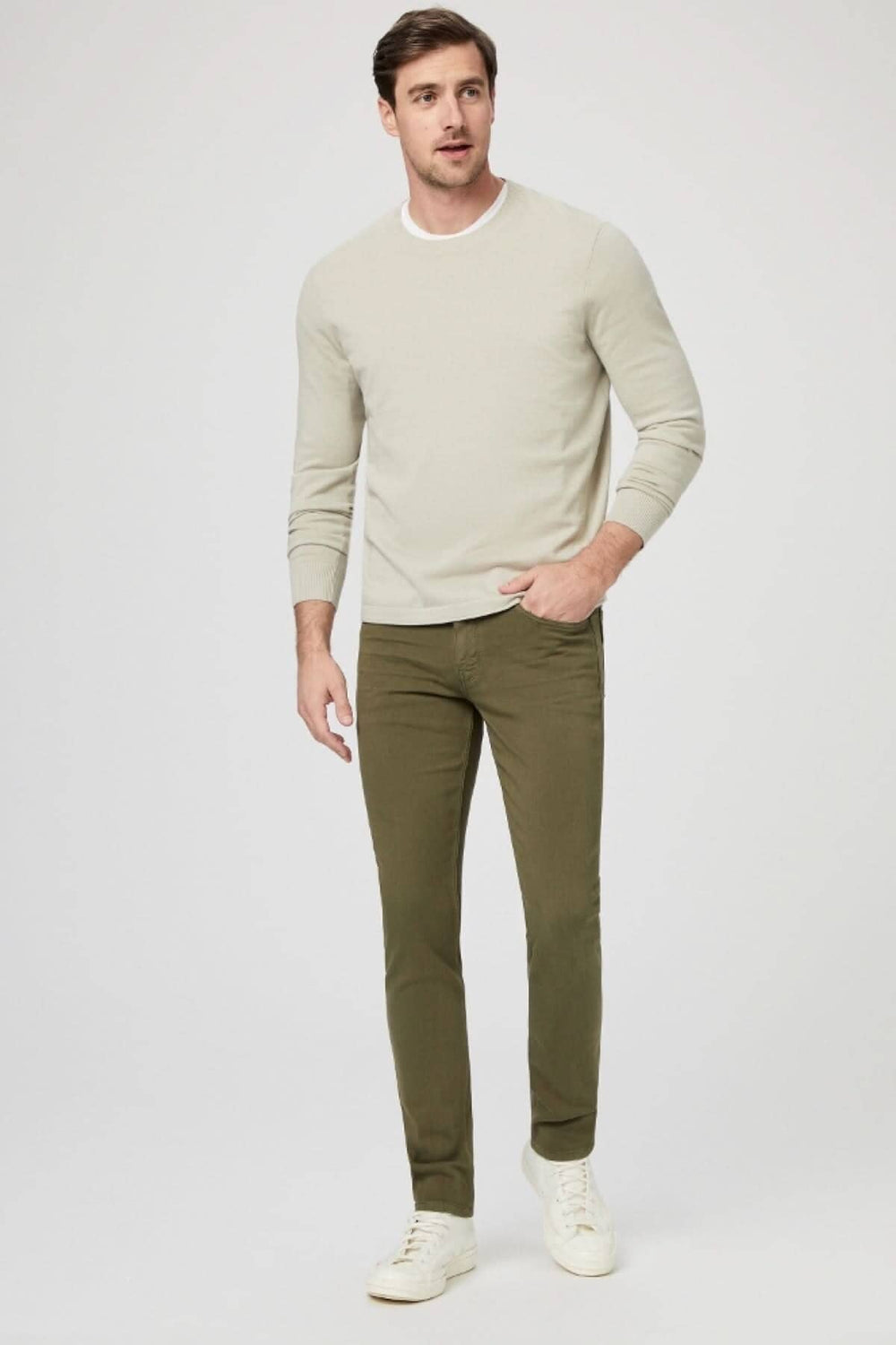 Homme portant un pull beige et un jean vert armée, look moderne et décontracté, chaussé de baskets blanches.