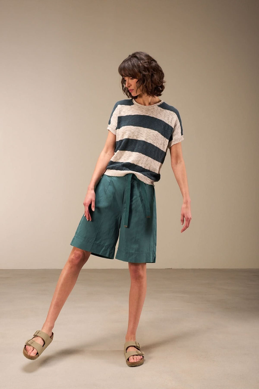 Femme portant un bermuda décontracté à taille ajustable, associé à un t-shirt rayé, dans un cadre minimaliste.