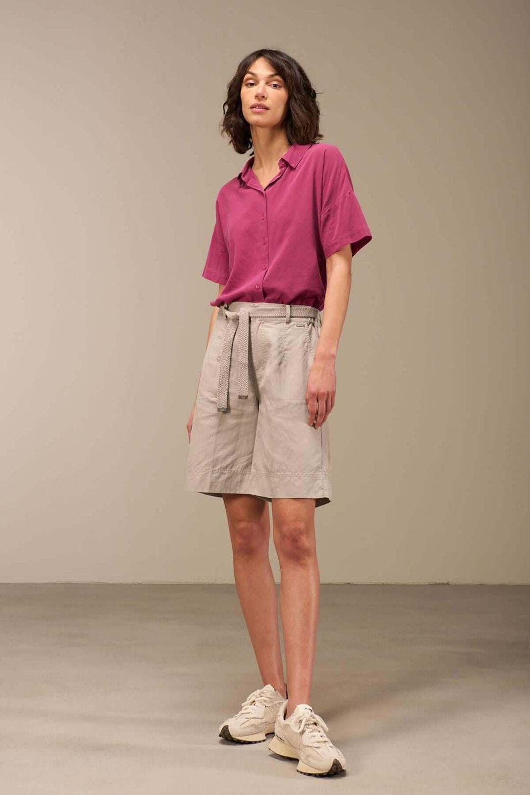 Femme en bermuda décontracté beige avec chemise rose, style bohème pour l'été.