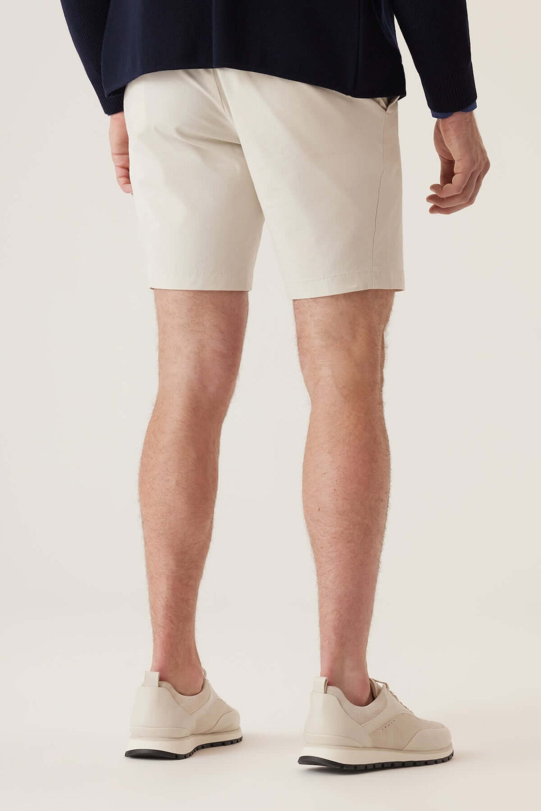 Homme de dos portant des bermudas extensibles en tissu beige, idéal pour un style décontracté et actif.