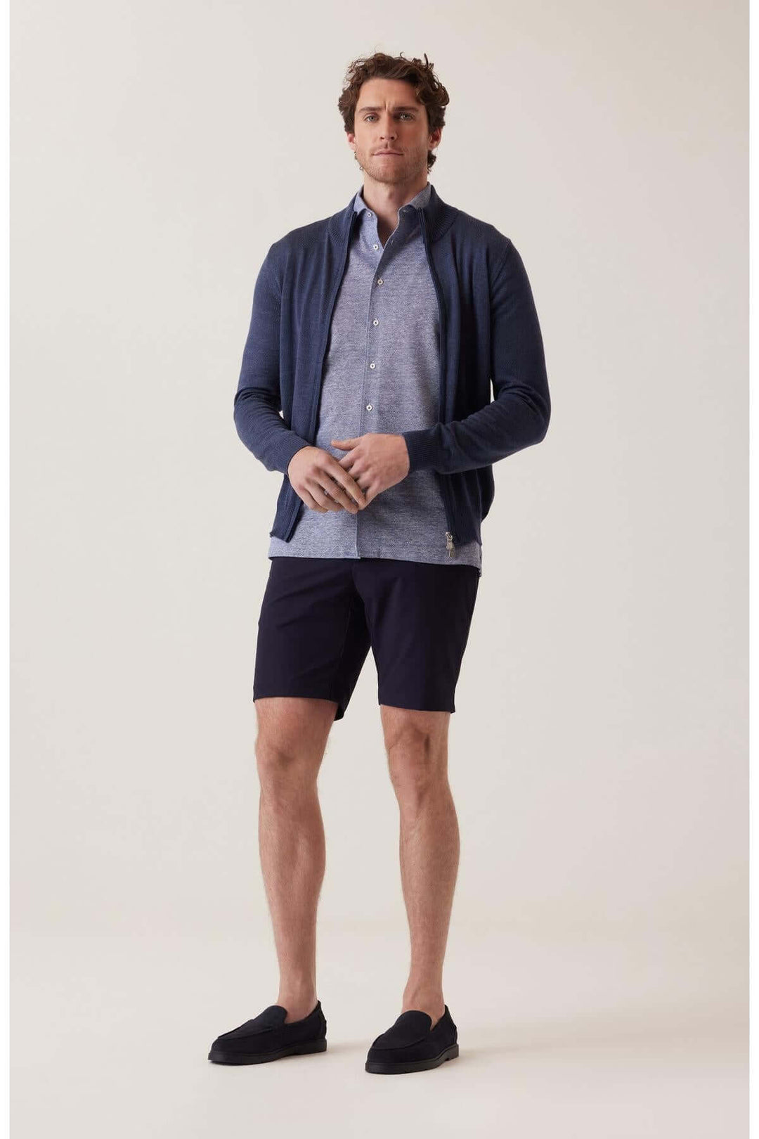 Homme en bermuda extensible et cardigan, portant une chemise décontractée pour un style élégant et confortable.