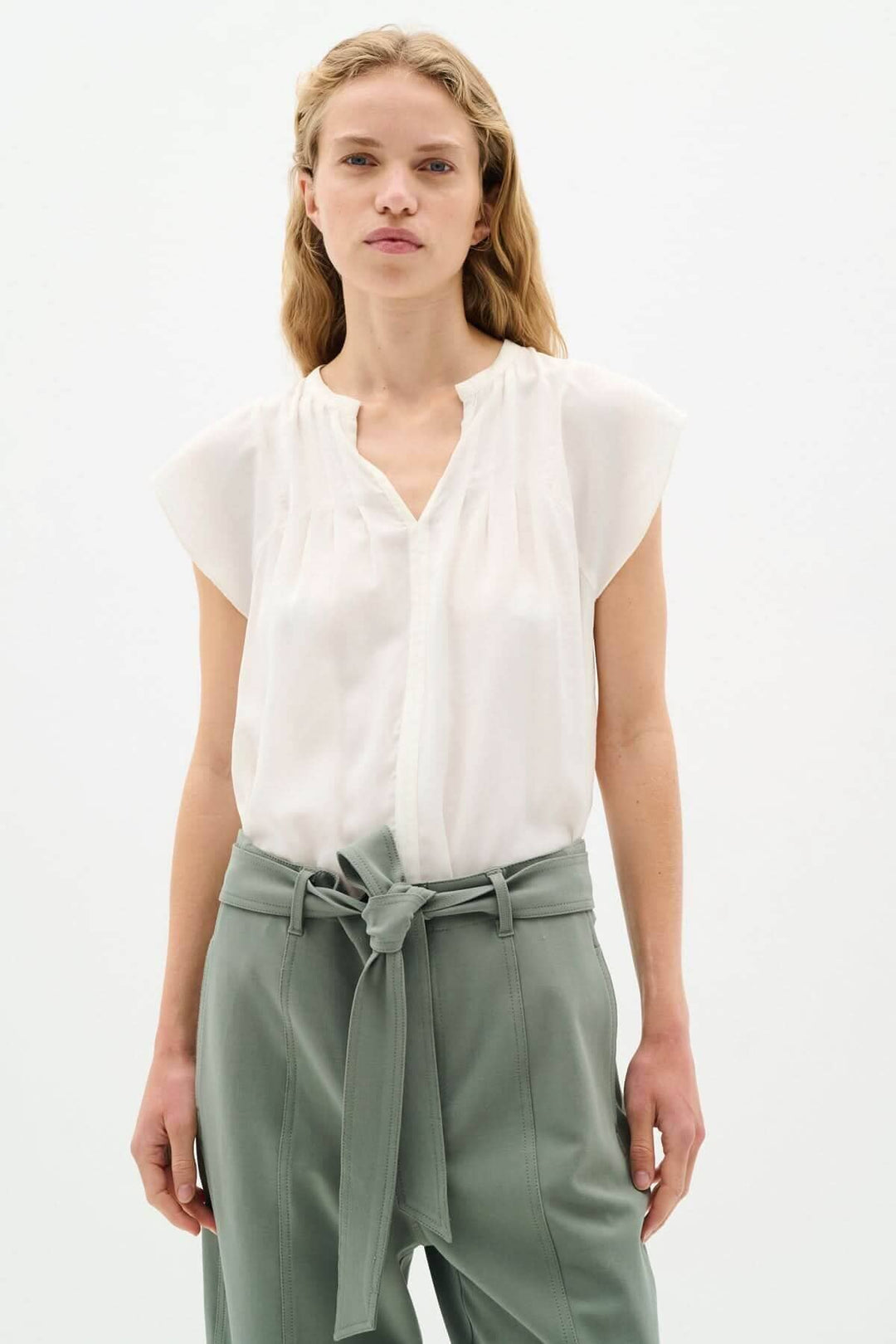 Blouse Cidenza légère et fluide avec encolure plissée et manches volantes, portée avec un pantalon taille haute.