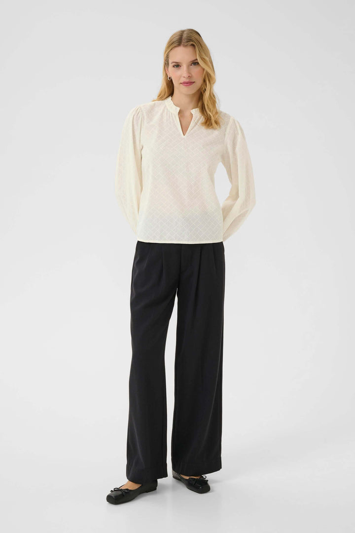 Alt Tag: Blouse Eimy féminine avec motif discret, encolure fendue et manches longues bouffantes, portée avec un pantalon noir élégant.