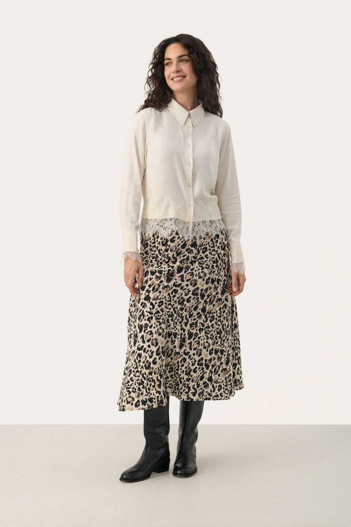 Femme portant une blouse Lenina élégante avec dentelle, associée à une jupe léopard longue et des bottes noires.