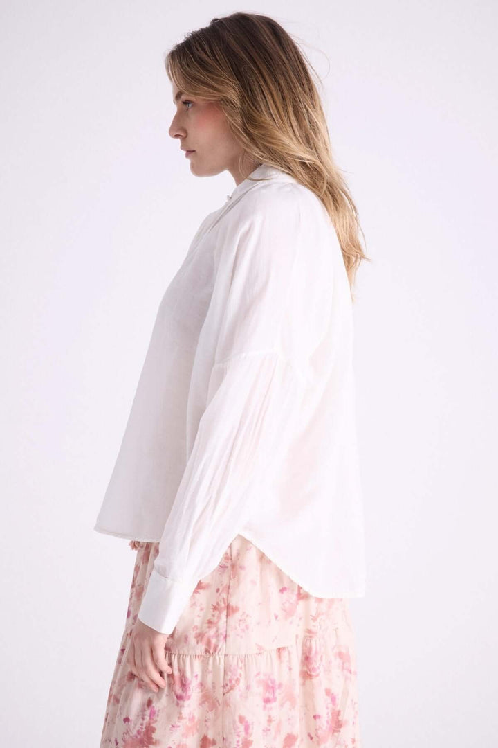 Blouse légère à capuche avec cordons à pompons, parfaite pour les journées estivales, portée avec une jupe fleurie.