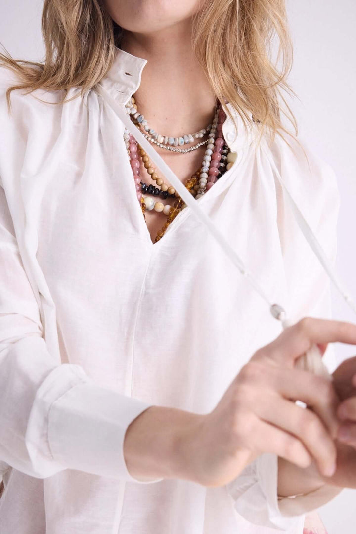Blouse légère blanche à capuche avec cordons, accessorized avec des colliers colorés, esprit bohème.