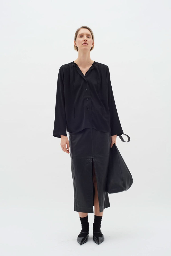 Modèle portant une blouse noire à manches longues et jupe en cuir, look chic et élégant.