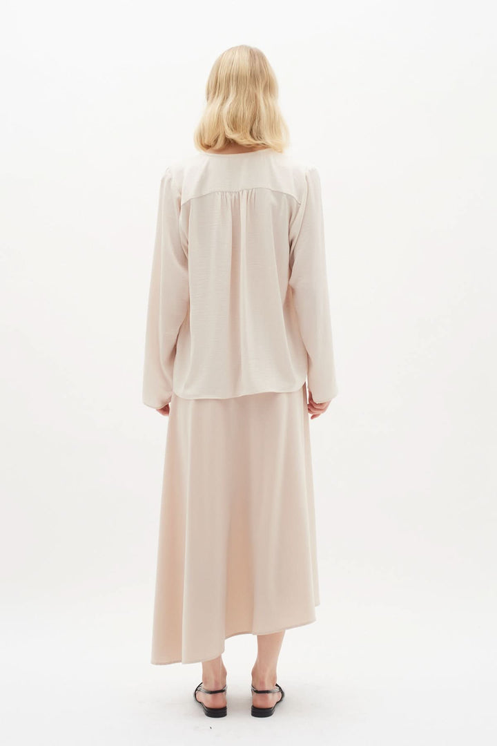 Blouse Mato, chemise classique à manches longues, encolure nouée, portée avec une jupe légère, couleur beige.