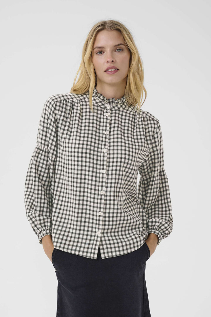 Blouse Samilla à carreaux avec col à volants, manches bouffantes et boutonnage frontal, portée par un modèle pour un look chic et intemporel.