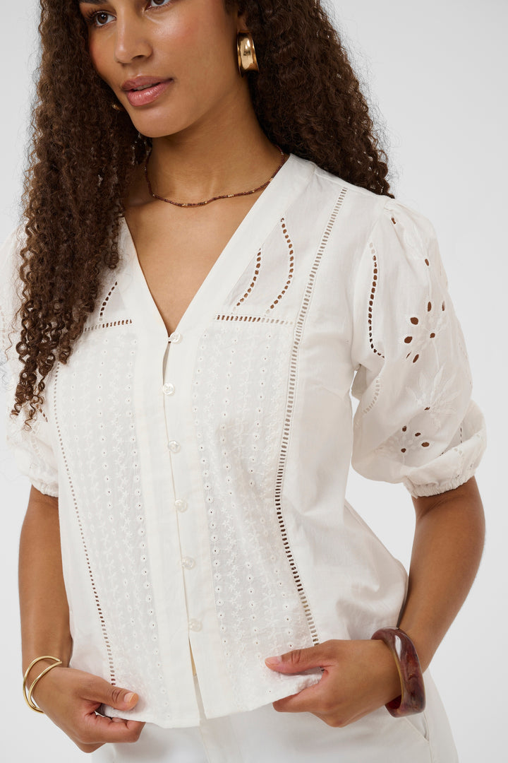 Blouse Signe avec détails ajourés et broderies, encolure en V, chic et féminine, portée par un modèle