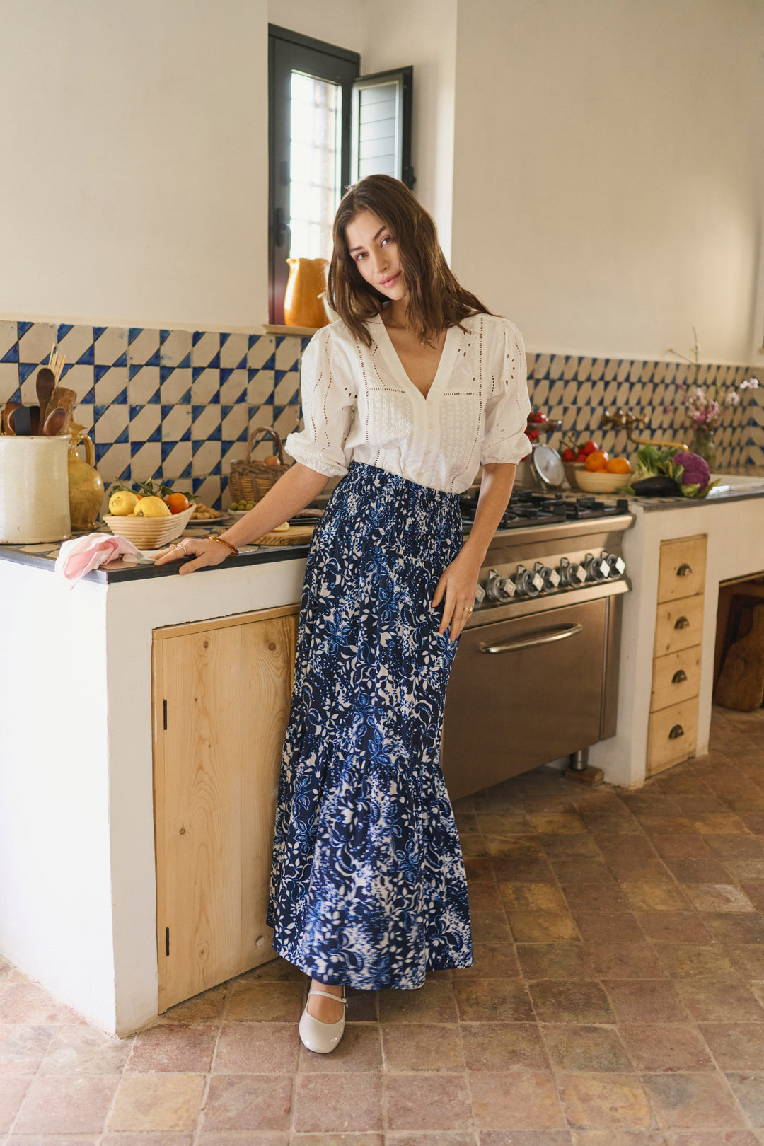 Femme portant la Blouse Signe, détails ajourés et broderies, encolure en V, dans une cuisine rustique.