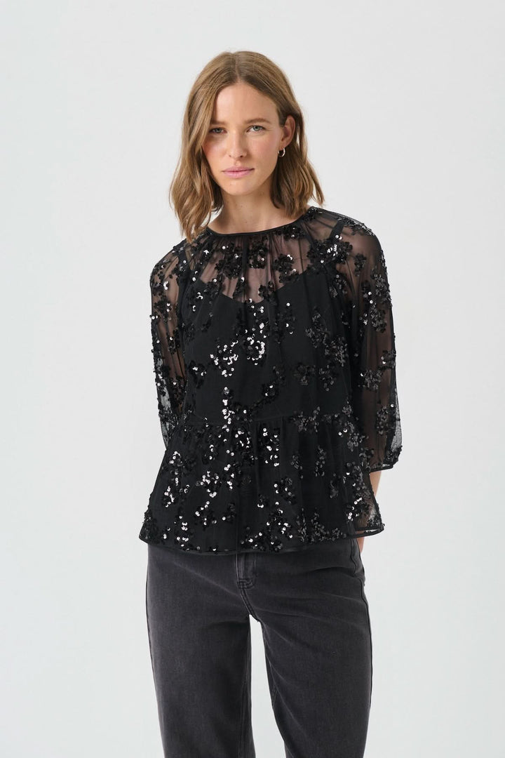 Femme portant la Blouse Vivan à sequins floraux avec manches trois-quarts et base en tulle, élégante pour une tenue chic et moderne.