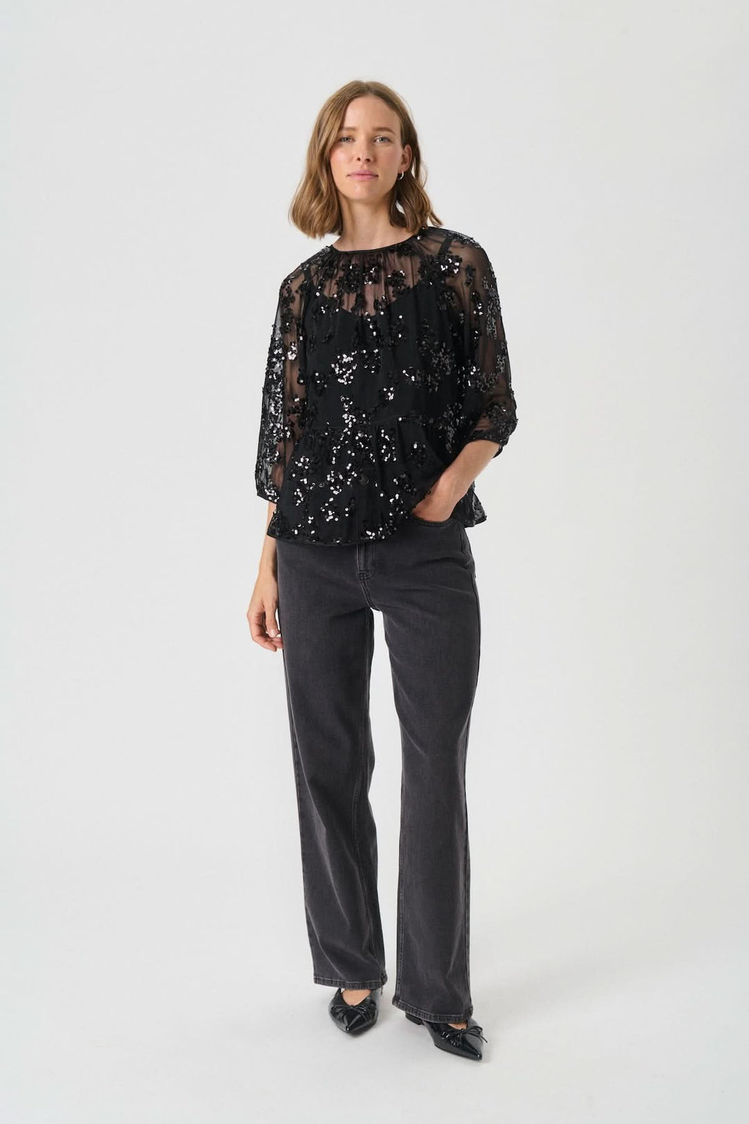 Blouse Vivan à sequins floraux avec manches trois-quarts, portée avec un pantalon noir pour un look chic et sophistiqué.