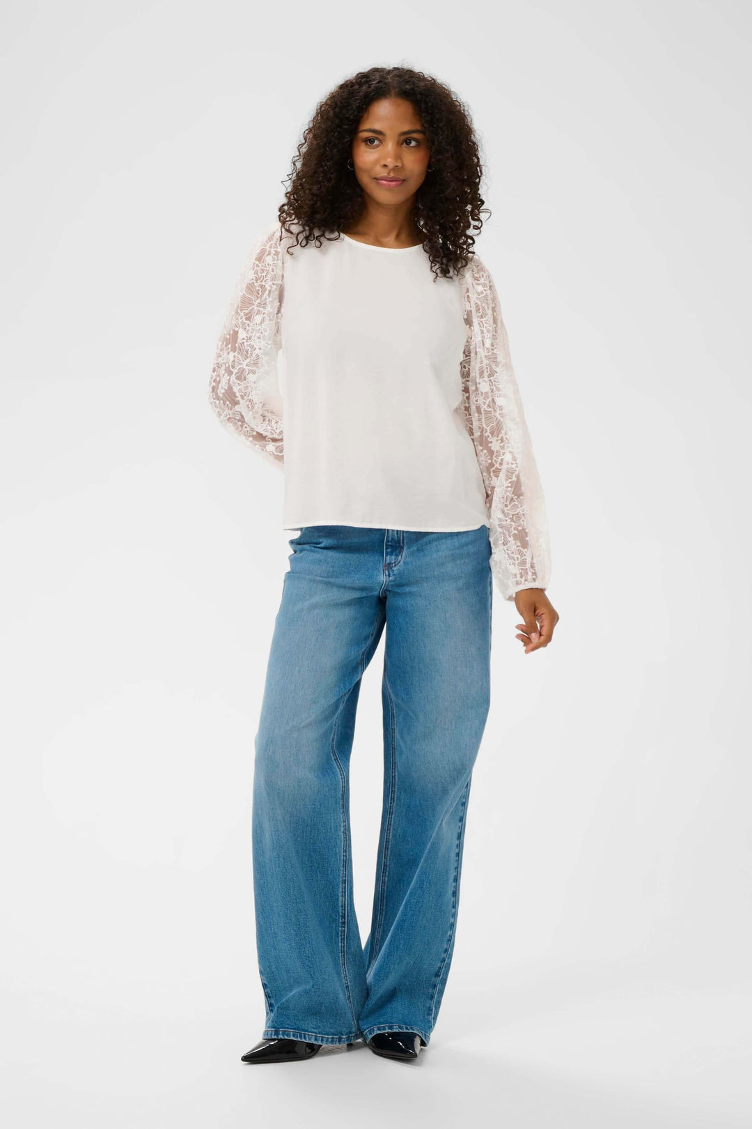 Femme portant une "Blouse avec broderie" en dentelle, manches longues, avec jean, style élégant et décontracté.