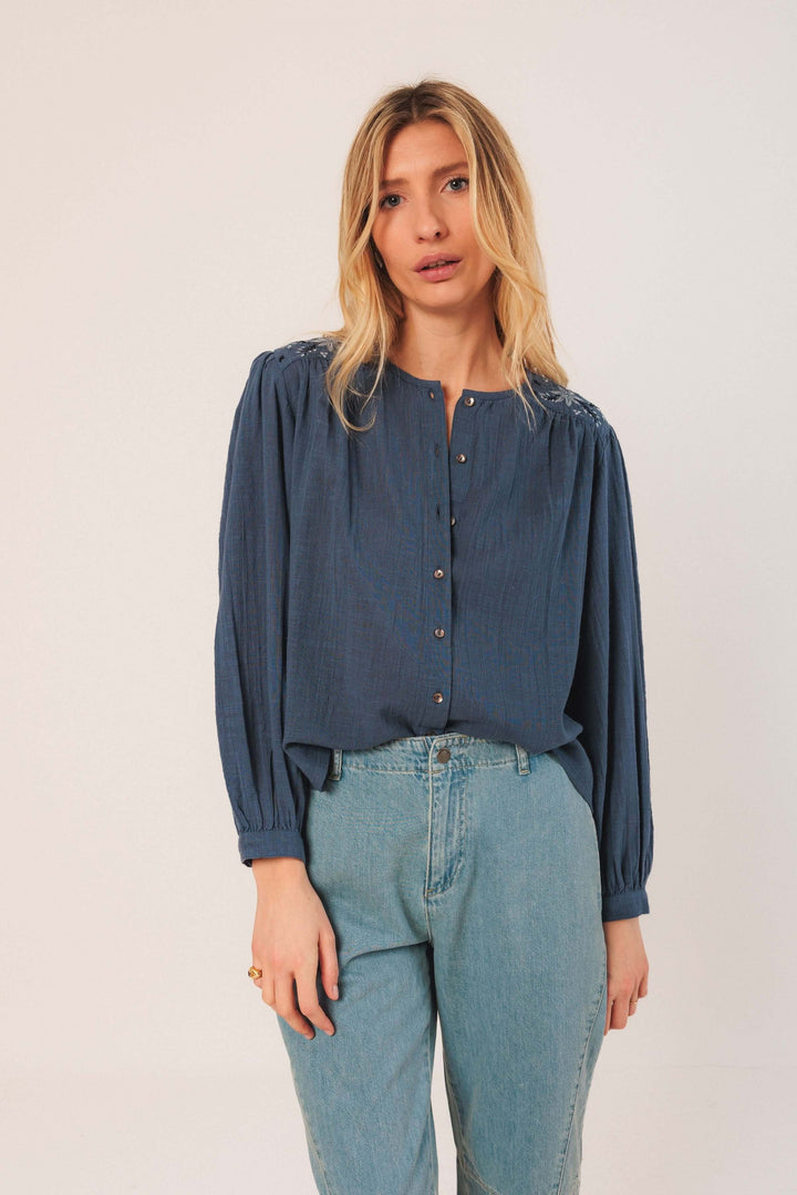 Blouse brodée bleue avec encolure ronde, manches bouffantes et boutons, portée avec jean taille haute.