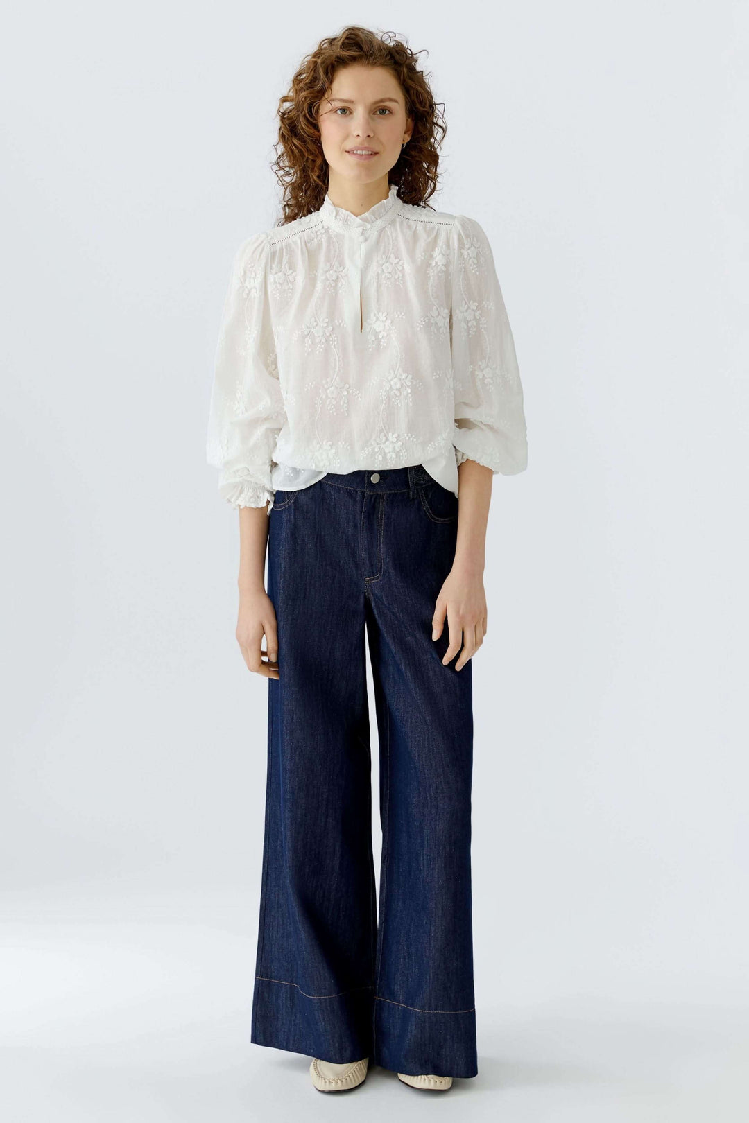Blouse à broderies florales portée par une femme, style élégant avec col montant et manches bouffantes, idéale pour diverses occasions.