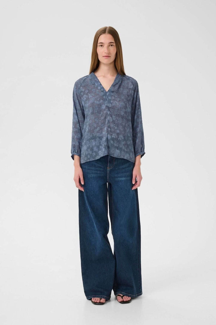 Blouse à col V et manches 3/4, portée avec un jean pour un look chic décontracté.