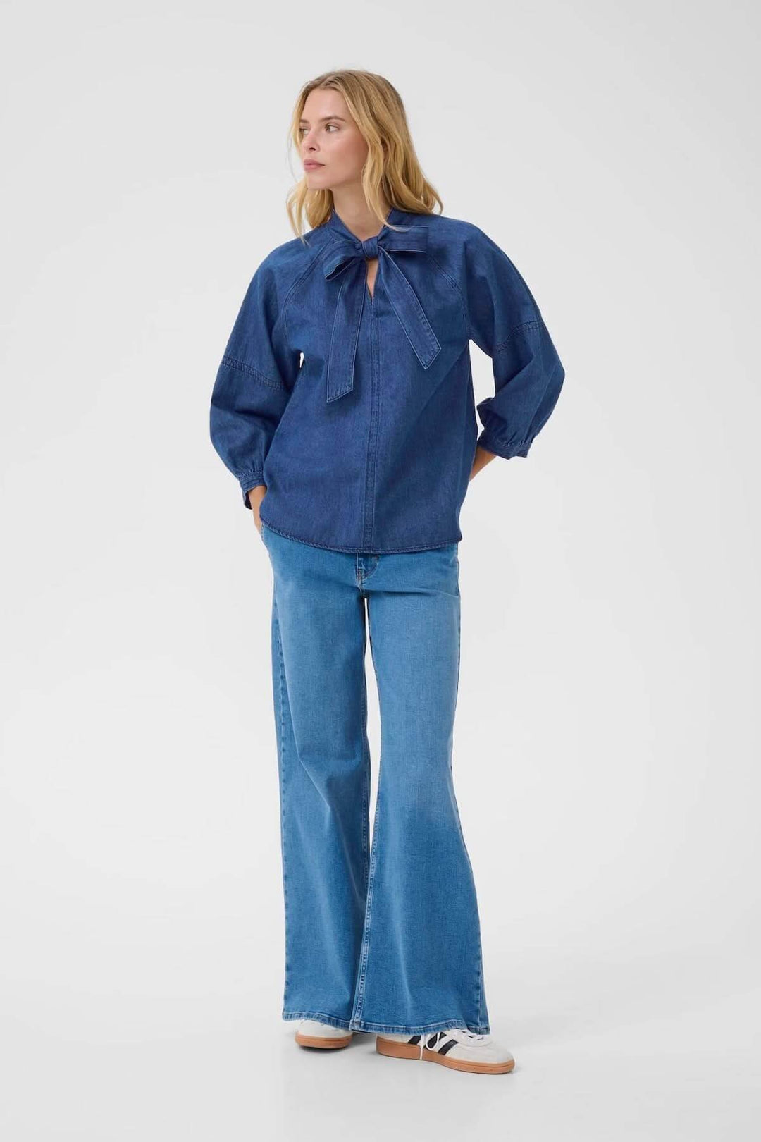 Femme portant une blouse en denim avec col lavallière et manches bouffantes, mode décontractée et élégante.