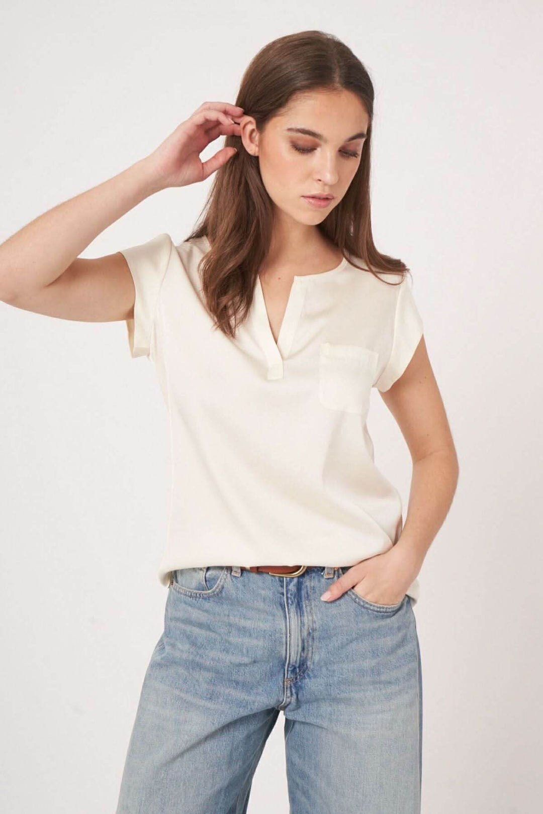 Femme portant un t-shirt beige à col en V et poche, avec un style décontracté et élégant, associé à un jean.