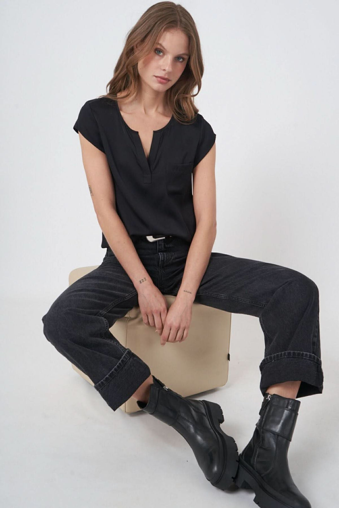 Blouse en soie noire avec décolleté en V, portée par un mannequin assis sur un tabouret.