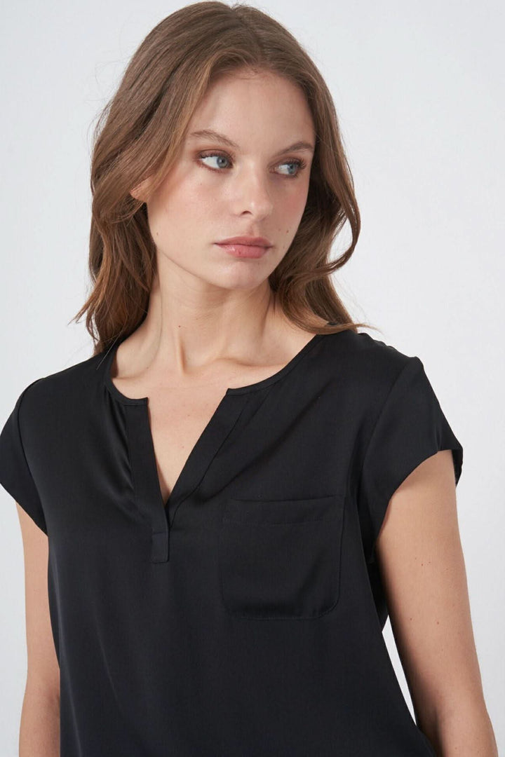 Femme portant une blouse en soie noire avec décolleté en V et poche plaquée, style élégant et décontracté.