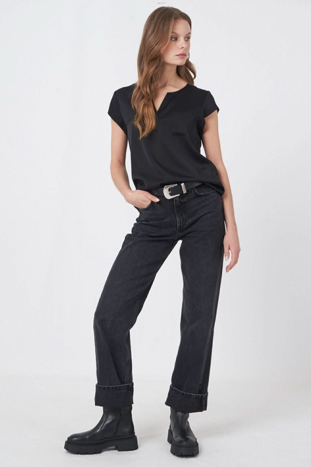 Modèle portant une blouse noire à encolure V, avec jean noir et bottes, affichant un style décontracté et élégant.
