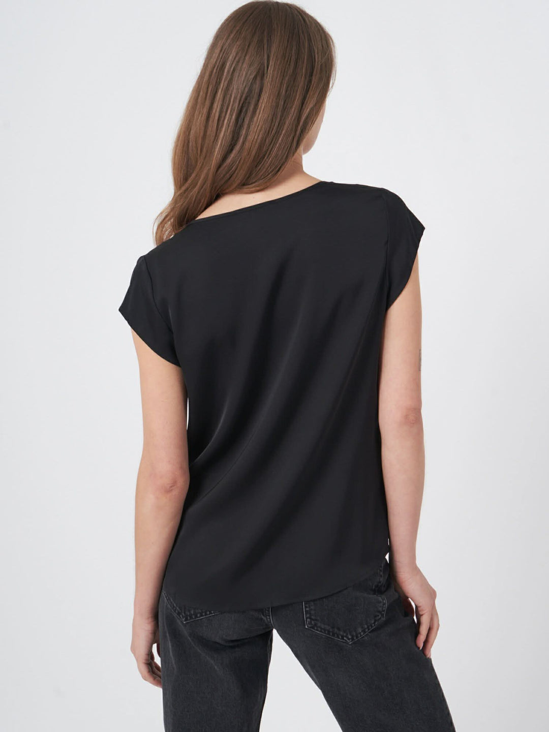 Blouse en soie noire légère avec manches coupées, dos de mannequin en pose décontractée.