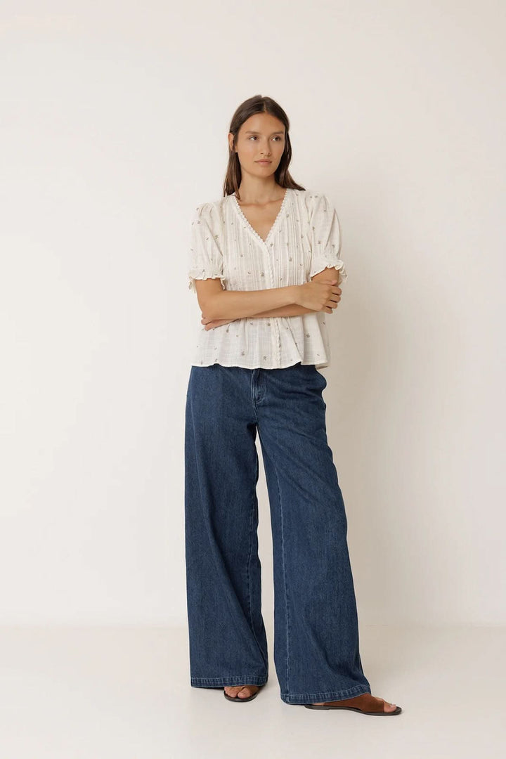 Femme portant une Blouse à encolure dentelle avec manches bouffantes et plis verticaux, accompagnée d'un jean ample.