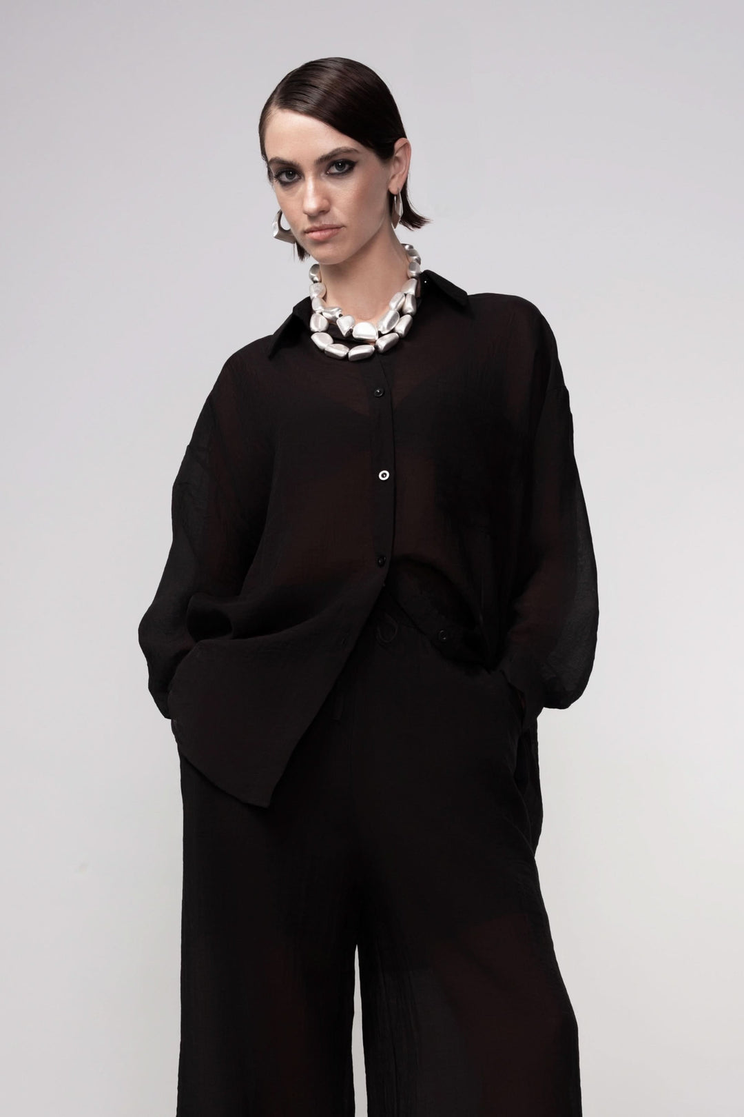 Femme portant une blouse fluide coupe ample noire avec col chemise, manches longues boutonnées, idéale pour une tenue élégante et décontractée.
