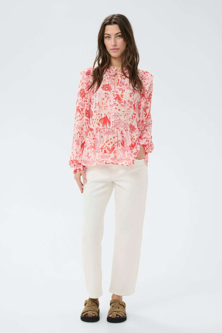 Blouse fluide à encolure fendue Alfrida avec imprimé délicat, associée à un pantalon blanc, confort et élégance quotidienne.