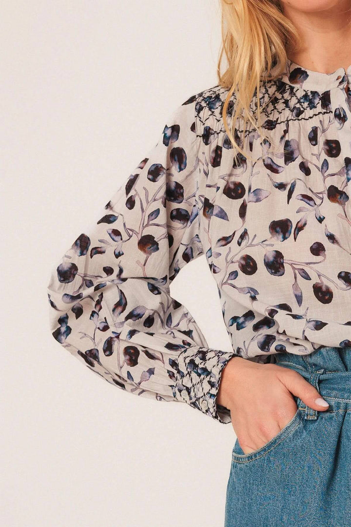 Blouse fluide à imprimé nature avec encolure boutonnée, détails smockés aux épaules et poignets, portée avec un jean.