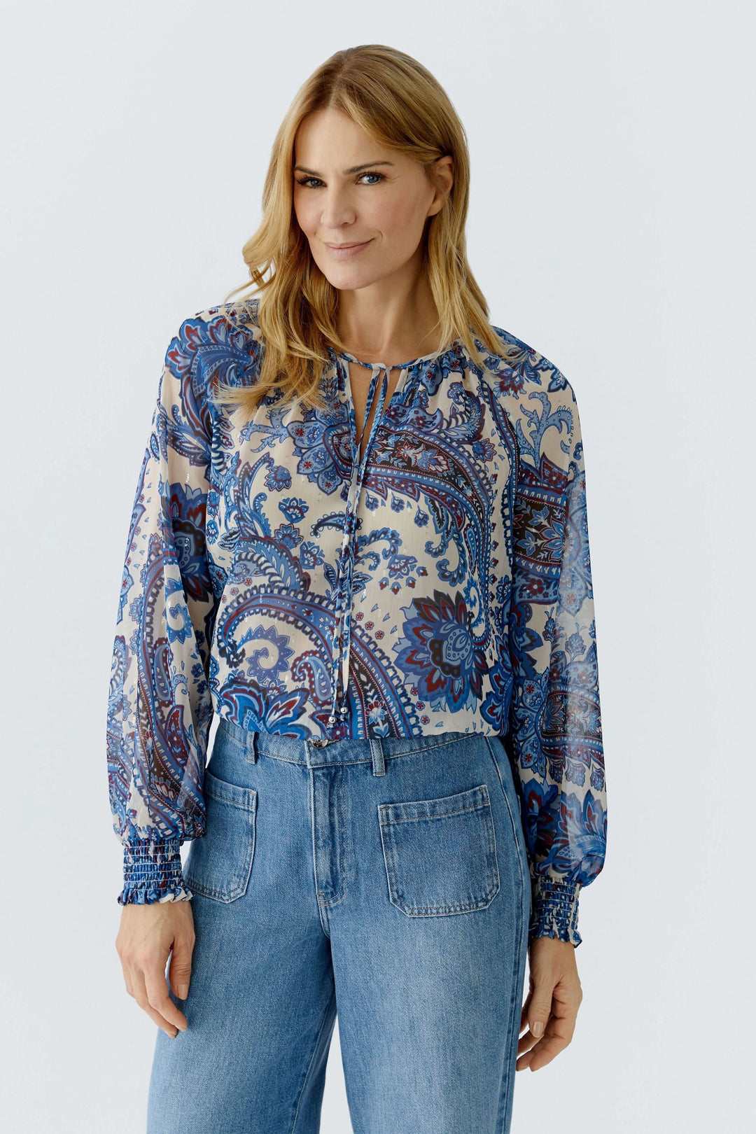 Blouse imprimée à manches longues avec motif cachemire, encolure fendue et matière légère, portée par une femme en jeans.