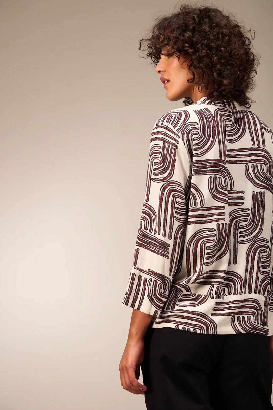 Femme portant une blouse à manches 3/4 avec motif graphique et encolure ronde, vue de dos, style décontracté et moderne.