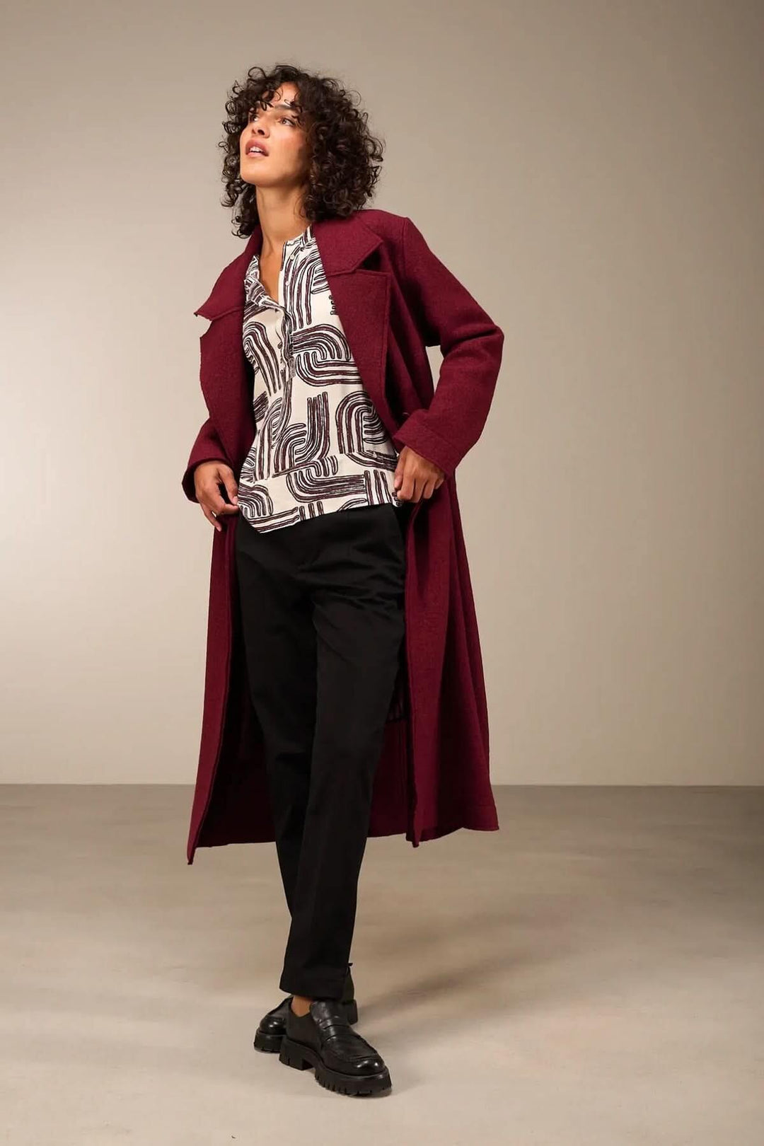 Femme portant une blouse à manches 3/4 décontractée avec encolure ronde, associée à un long manteau bordeaux pour un look élégant.