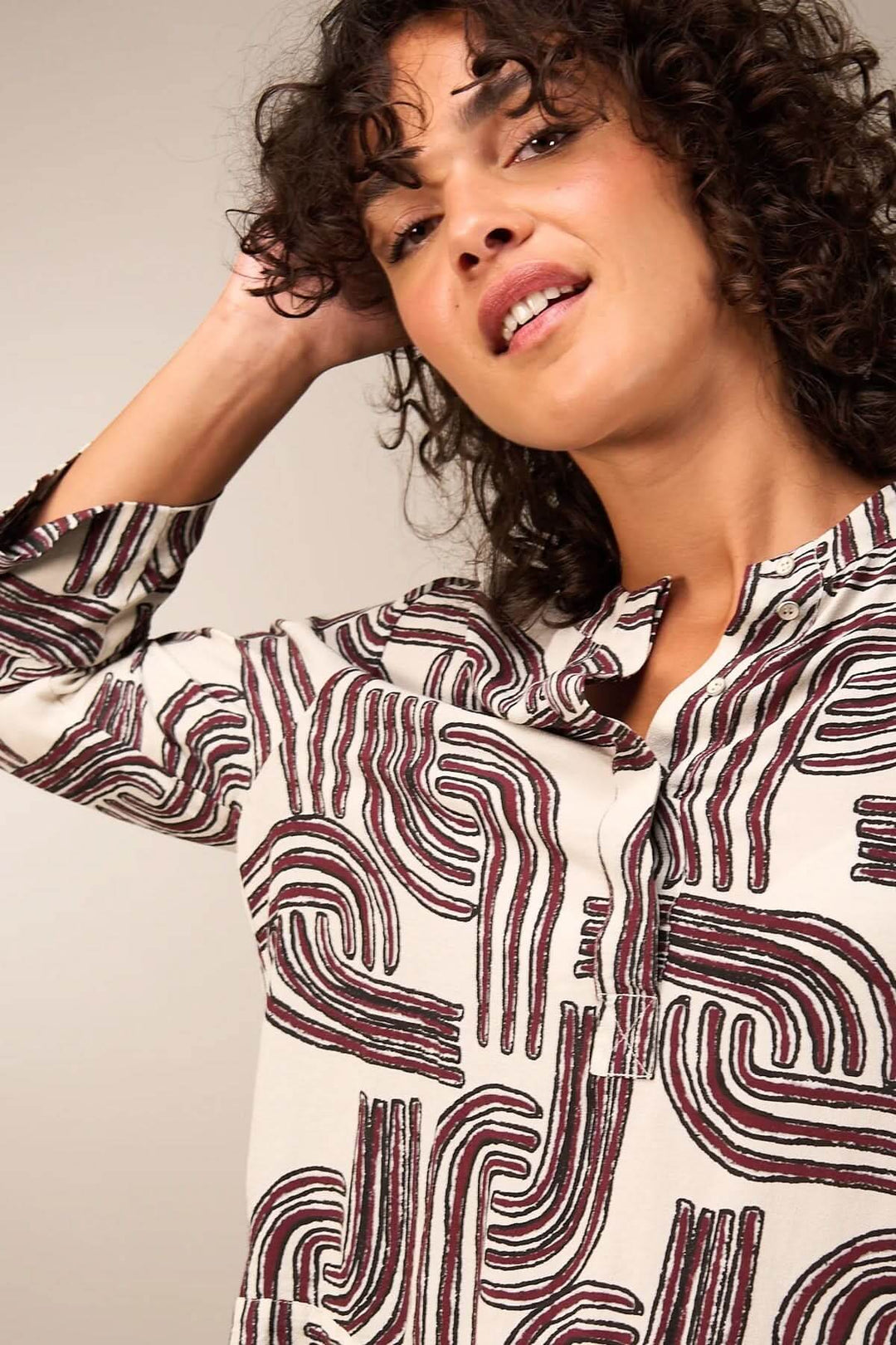 Femme portant une blouse à manches 3/4 avec motif abstrait, encolure ronde et patte boutonnée, alliant élégance et décontraction.