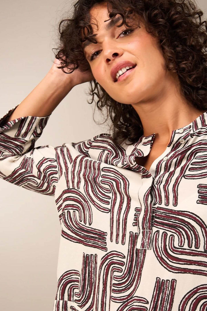 Femme portant une blouse à manches 3/4 avec motif abstrait, encolure ronde et patte boutonnée, alliant élégance et décontraction.