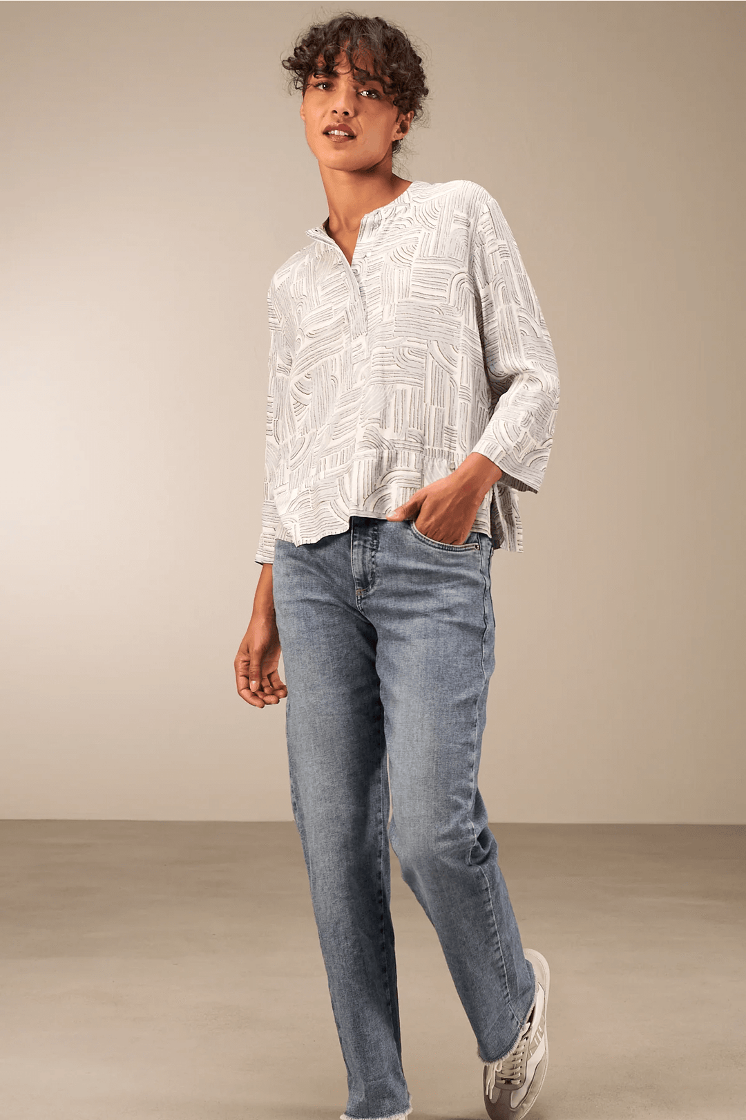 Femme portant une blouse à manches 3/4 avec encolure ronde et jean, style décontracté chic, fond neutre.