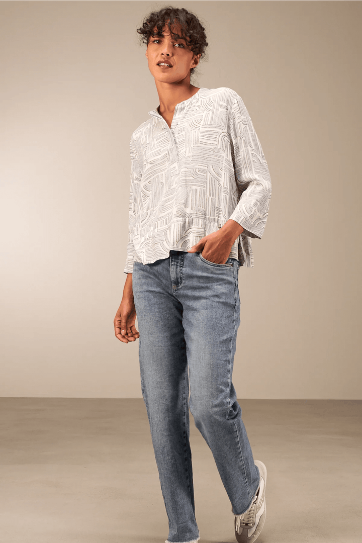 Femme portant une blouse à manches 3/4 avec encolure ronde et jean, style décontracté chic, fond neutre.