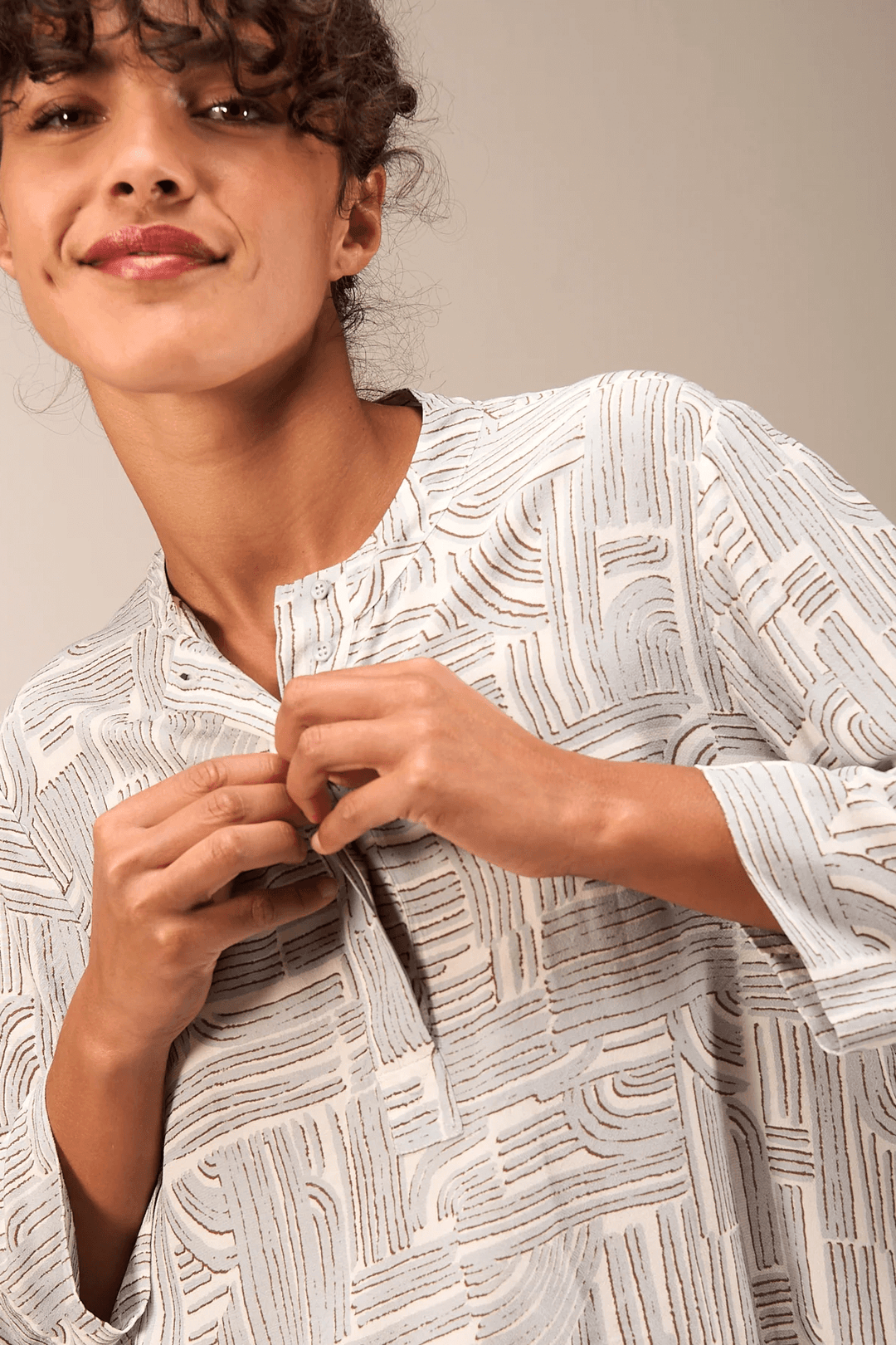 Femme portant une blouse à manches 3/4 avec encolure ronde et patte boutonnée, tissu fluide, style décontracté et moderne.