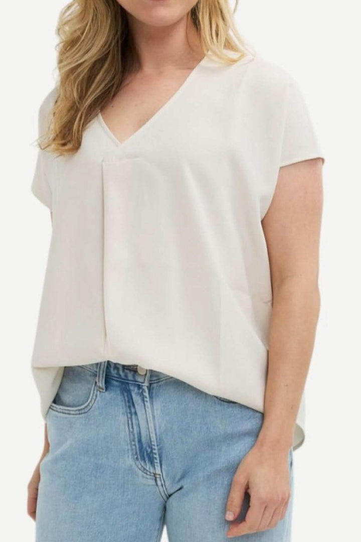 Blouse à manches courtes, col en V, coupe ample et fluide, portées avec un jean, style élégant et décontracté.