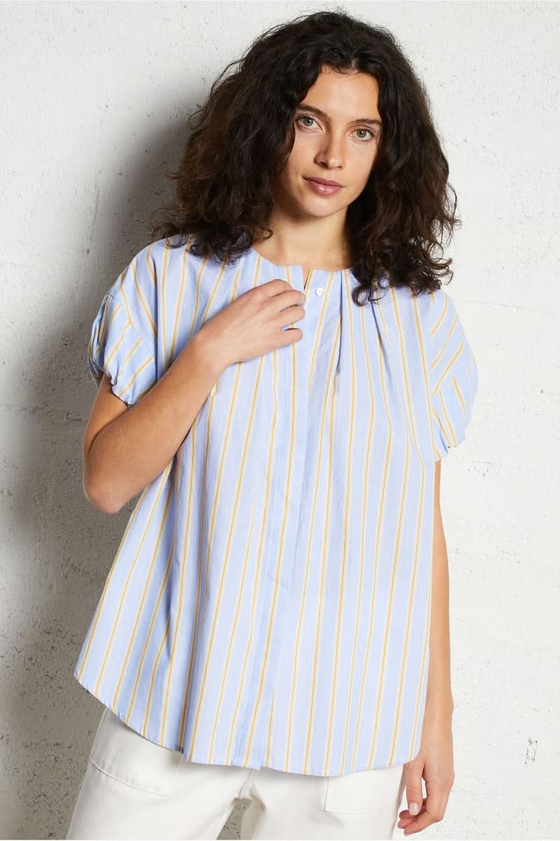 Femme portant une blouse oversize à rayures, coupe ample et manches courtes, offrant un style épuré et élégant. Décris moi le produit en français.